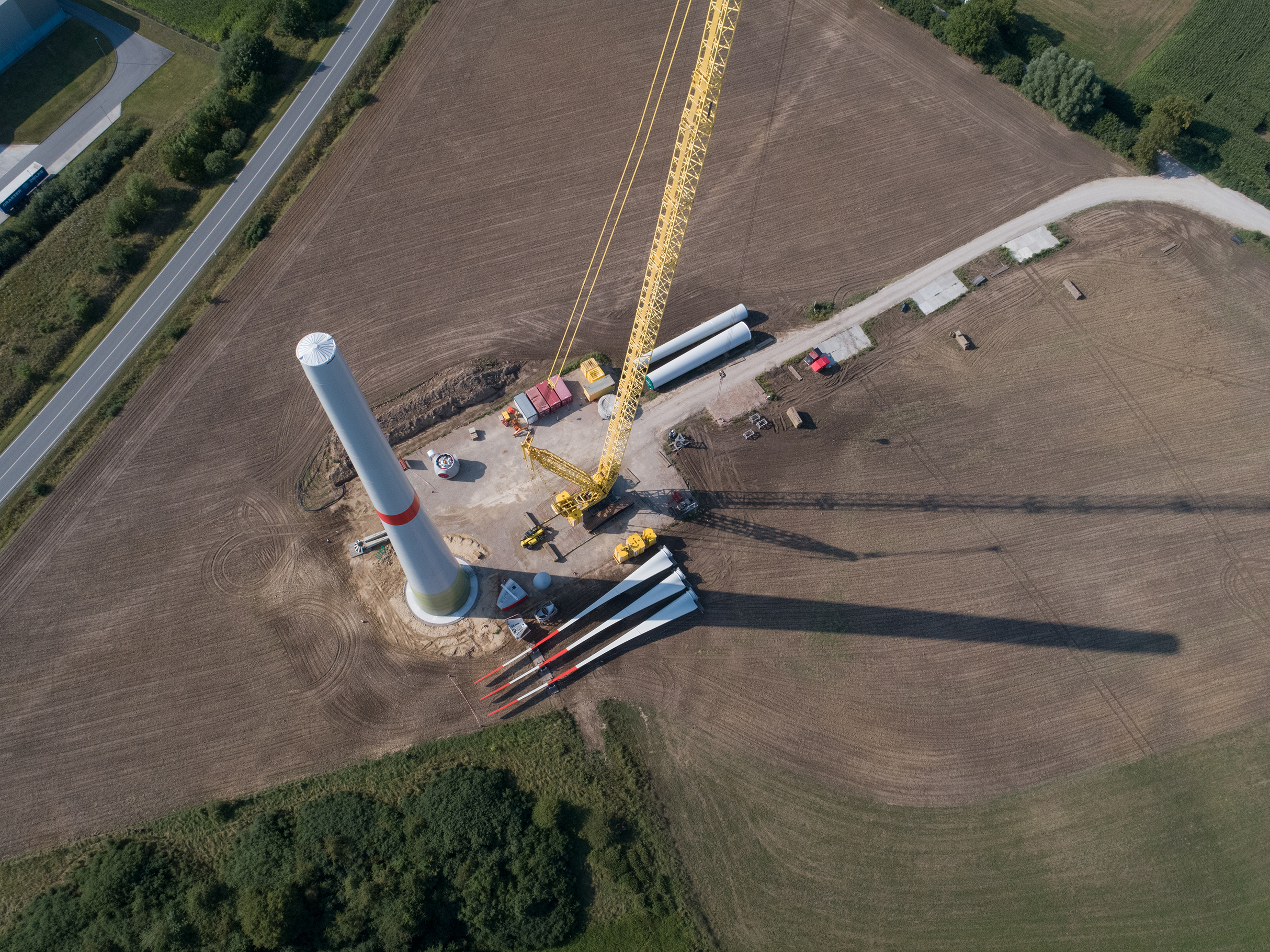 Das Bild zeigt eine Windenergieanlage im Aufbau. Zu sehen ist der untere Teil des Turms. Daneben steht ein Kran.